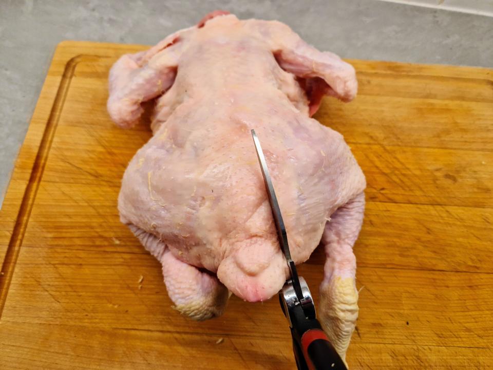 pair of scissors cutting into a whole chicken on a cutting board