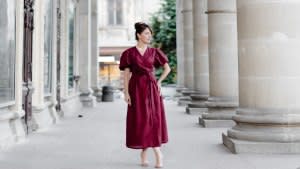 Woman in red dress is walking on street on old building background.