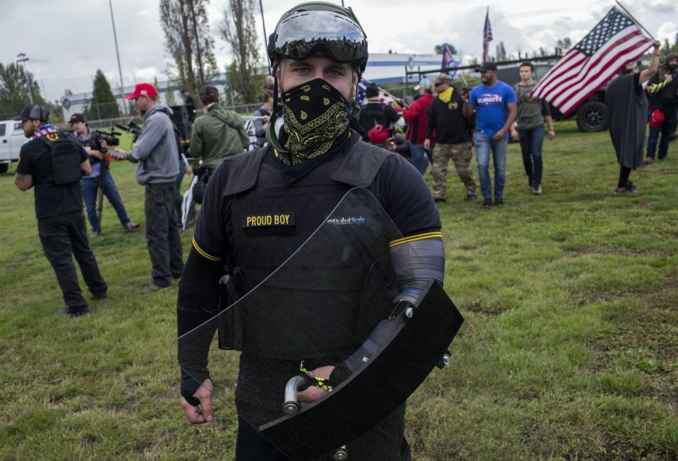 Picture of a man wearing military gear and the name 'Proud Boys' with an American flag in background