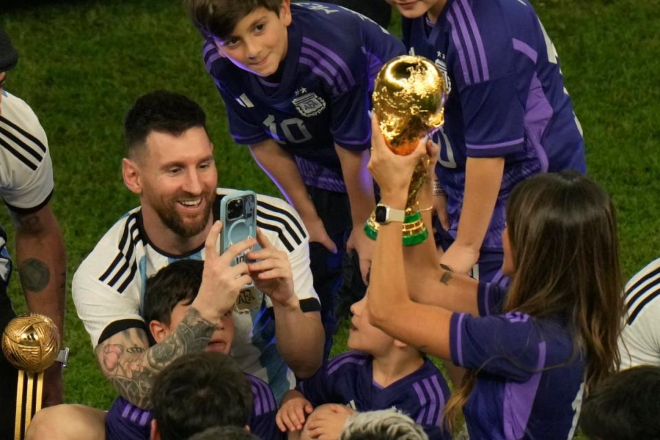 Argentina's Lionel Messi takes pictures of his wife Antonela Roccuzzo as she holds the winners trophy after Argentina won the World Cup final soccer match against France at the Lusail Stadium in Lusail, Qatar, (AP)