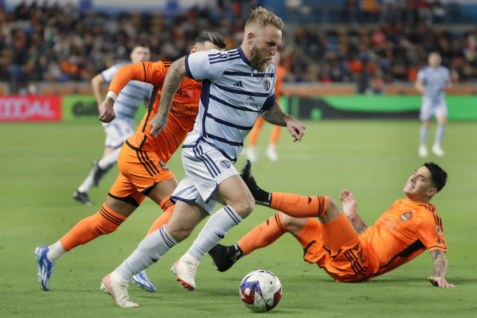 Sporting Kansas City forward Johnny Russell, center, moves the ball in front of Houston Dynamo midfielder Amine Bassi, left, as defender Franco Escobar, right, falls backward on the chase during the first half of an MLS playoff soccer match, Sunday, Nov. 26, 2023, in Houston. (AP Photo/Michael Wyke)