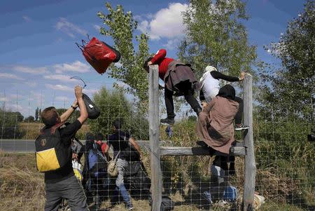 Migrants jump over a road protection fence as they leave a collection point in the village of Roszke, Hungary September 9, 2015. REUTERS/Marko Djurica