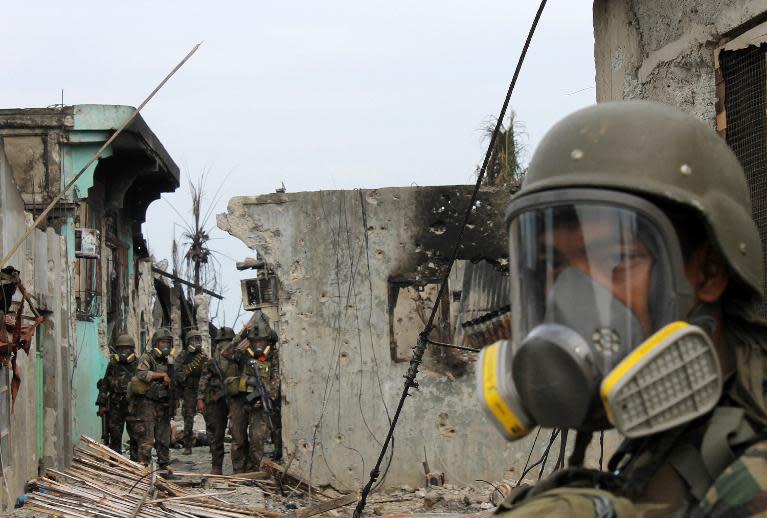 Soldiers wear gas masks due to the smell of decaying bodies as they patrol on September 26, 2013 among destroyed houses at the site of fighting between government forces and Moro Liberation Front rebels in the Santa Catalina area of Zamboanga City