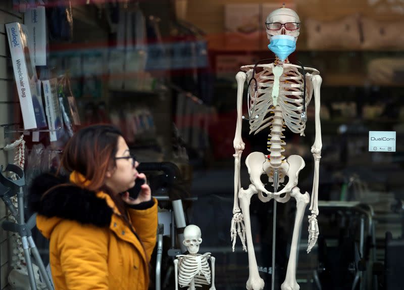 A woman walks past a mannequin wearing a protective mask in the window of a medical equipment supply store in south London