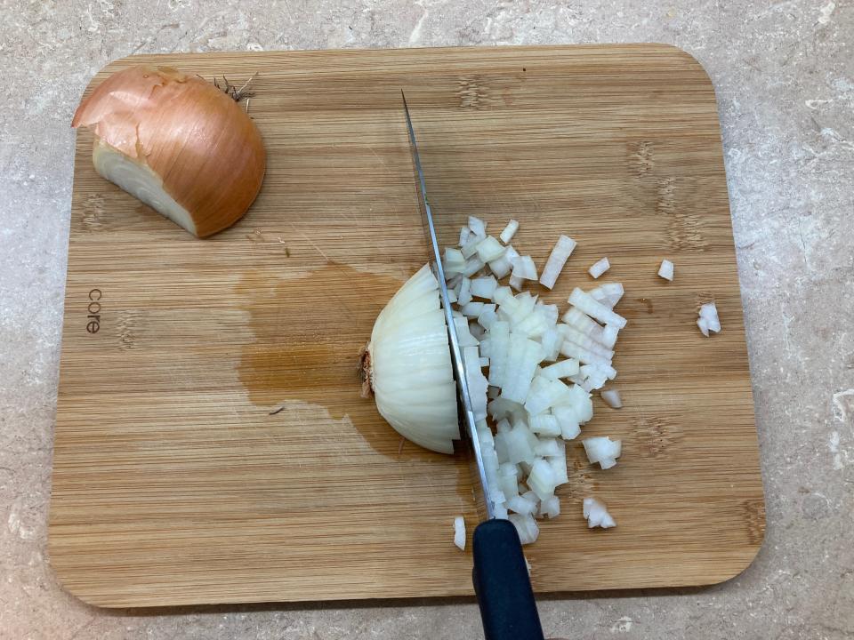 A cutting board with a half-diced onion on it.