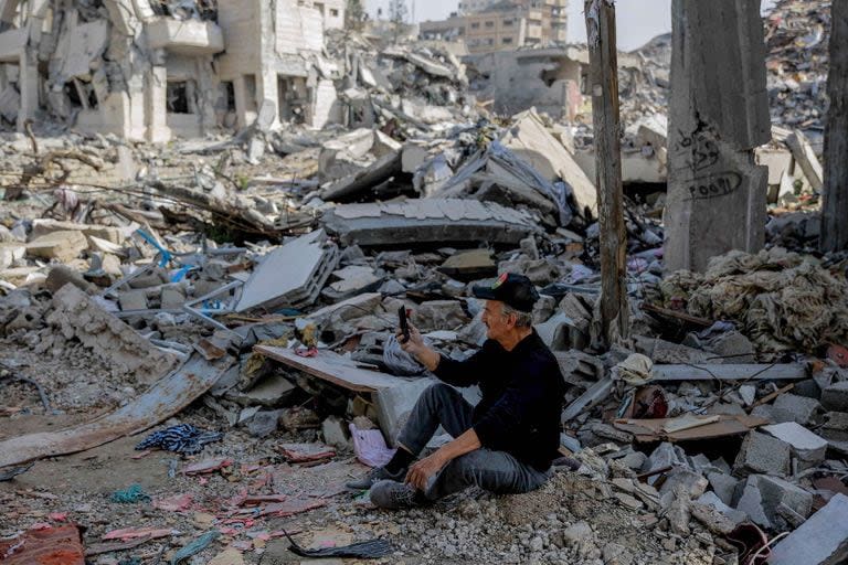 Un palestino utiliza su teléfono mientras está sentado entre los escombros de los edificios destruidos en la ciudad de Gaza, en el norte de la Franja de Gaza, tras semanas de bombardeos israelíes