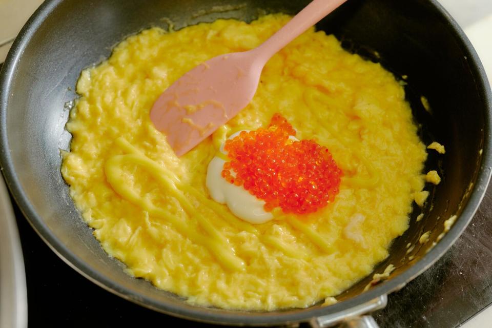 A French omelet cooks in a pan, topped with orange roe