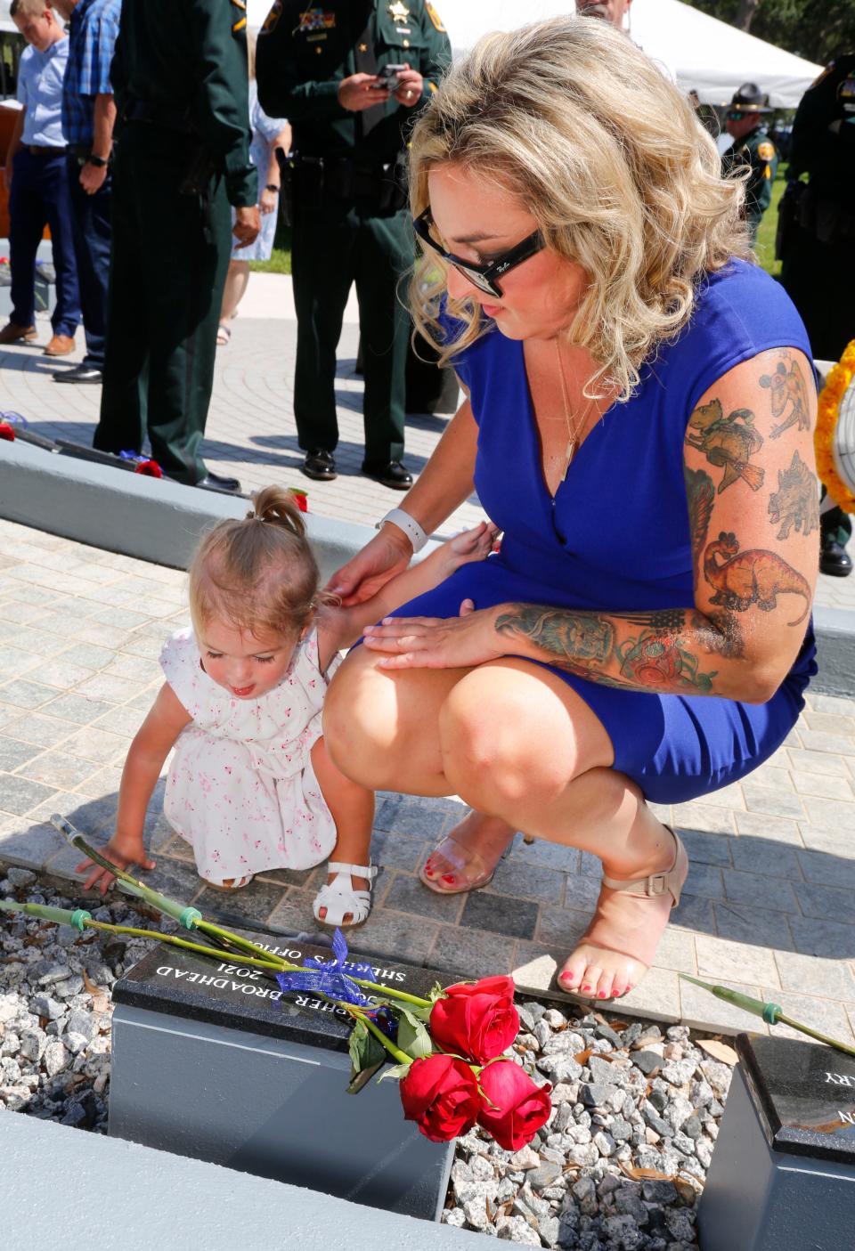 Elisa Broadhead looks on as her 1-year-old daughter, Reagan, adjusts the roses on the memorial plaque for her father, Polk County sheriff's Deputy Christopher Broadhead on Thursday. Broadhead died of COVID-19 in August after contracting the disease in the line of duty.
