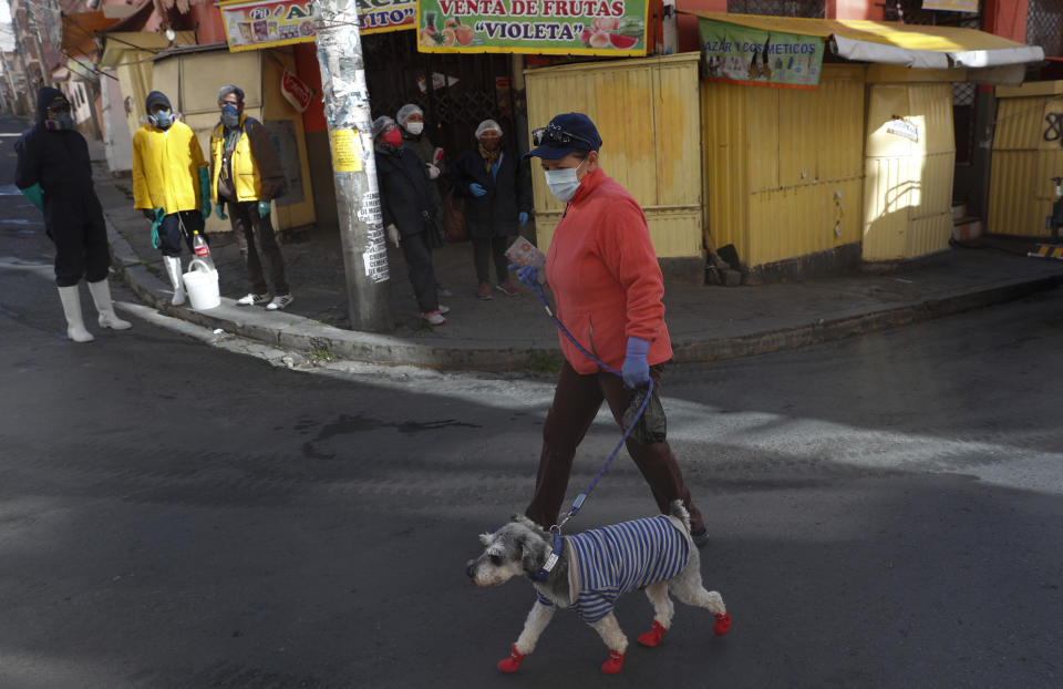 A woman wearing a mask to curb the spread of the new coronavirus walks her dog outside the Haiti market in La Paz, Bolivia, Tuesday, June 23, 2020. Health authorities say that a butcher at the marker died several weeks ago of COVID related symptoms, prompting its closure. (AP Photo/Juan Karita)