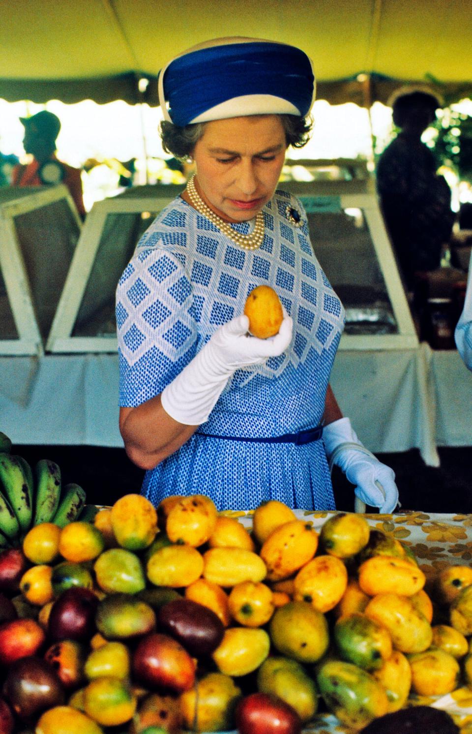 Queen Elizabeth ll picks up a mango as she tours a market in the British Virgin Islands in October of 1977.