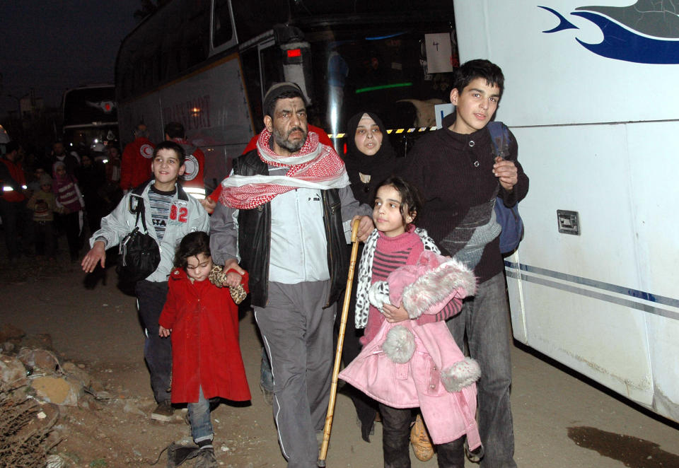 In this Sunday Feb. 9, 2014 file photo, released by the Syrian official news agency SANA, Syrian citizens walk towards a bus to evacuate them from the battleground city of Homs, Syria. Weeping children begged for food in the streets and women picked grass growing in the cracks of the sidewalks to eat as hunger gripped residents of rebel-held neighborhoods of the Syrian city of Homs blockaded for nearly two years by the military, according to a rare first-hand account by a man evacuated during a truce this week. (AP Photo/SANA, File)