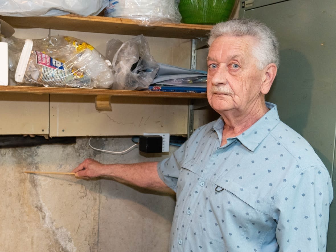 Robert Charbonneau points to an area of his home's foundation in the basement, where a slim crack runs a couple of metres. What appears to be water staining surrounds the crack. Charbonneau says he discovered the crack in spring 2021, after the Stage 2 LRT construction began nearby. (Jean Delisle/CBC - image credit)