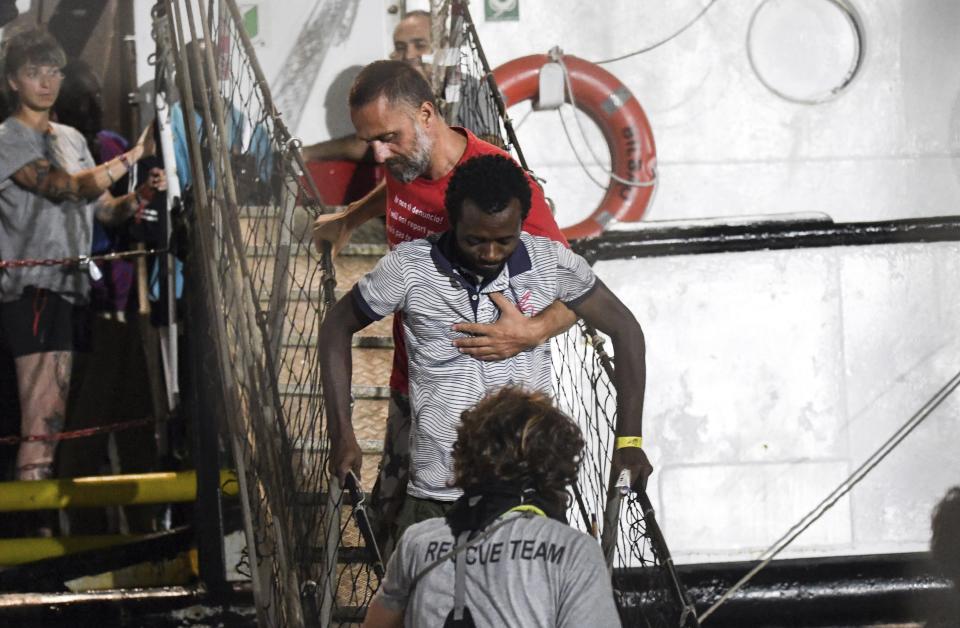 In this photo taken on Tuesday, Aug. 20, 2019, a man is helped disembark from the Open Arms rescue ship on the Sicilian island of Lampedusa, southern Italy. An Italian prosecutor ordered the seizure of a rescue ship and the immediate evacuation of more than 80 migrants still aboard, capping a drama Tuesday that saw 15 people jump overboard in a desperate bid to escape deteriorating conditions on the vessel and Spain dispatch a naval ship to try to resolve the crisis. (AP Photo/Salvatore Cavalli)