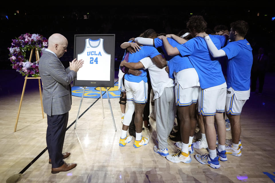 Members of the UCLA basketball team surround the family of Jalen Hill as head coach Mick Cronin, left, stands by during a ceremony for him prior to an NCAA college basketball game between UCLA and Denver Saturday, Dec. 10, 2022, in Los Angeles. Hill died on Sept. 20, 2022. (AP Photo/Mark J. Terrill)