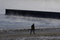 A man walks along the shore of Lake Michigan at the Lighthouse Beach in Evanston, Ill., Tuesday, Jan. 16, 2024. While the U.S. is shivering through bone-chilling cold, most of the rest of world is feeling unusually warm weather. Scientists Tuesday say that fits with what climate change is doing to Earth. (AP Photo/Nam Y. Huh)