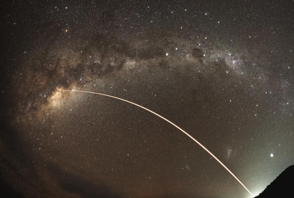 arc of a rocket launch at night, with the rocket disappearing into the sky and the milky way