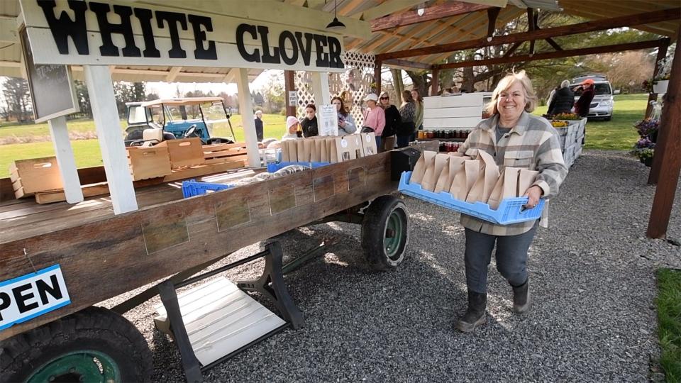 Linda Holden, Nate Riedy's mother-in-law, carries warm pretzels to the White Clover Family Farm stand while people line up before it opens. The business was inspired by the locally sourced food movement, and spurred on by supply-chain issues that intensified during the pandemic.
