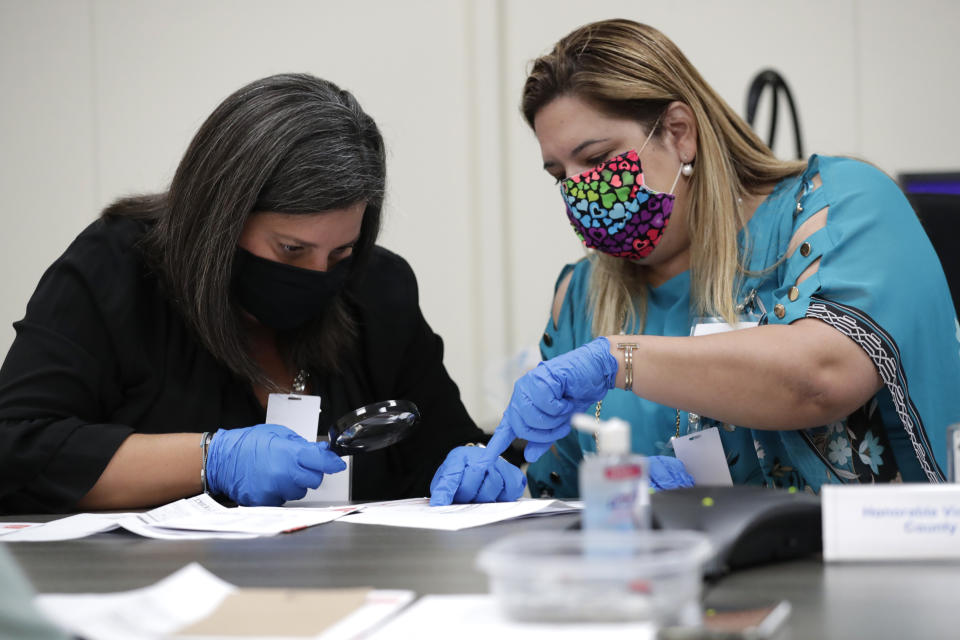 Miami-Dade County Judges Eleane Sosa-Bruzon, left, and Victoria Ferrer, right, examine signatures on vote-by-mail ballots for the August 18 primary election as the canvassing board meets at the Miami-Dade County Elections Department, Thursday, July 30, 2020, in Doral, Fla. President Donald Trump is for the first time publicly floating a "delay" to the Nov. 3 presidential election, as he makes unsubstantiated allegations that increased mail-in voting will result in fraud. (AP Photo/Lynne Sladky)