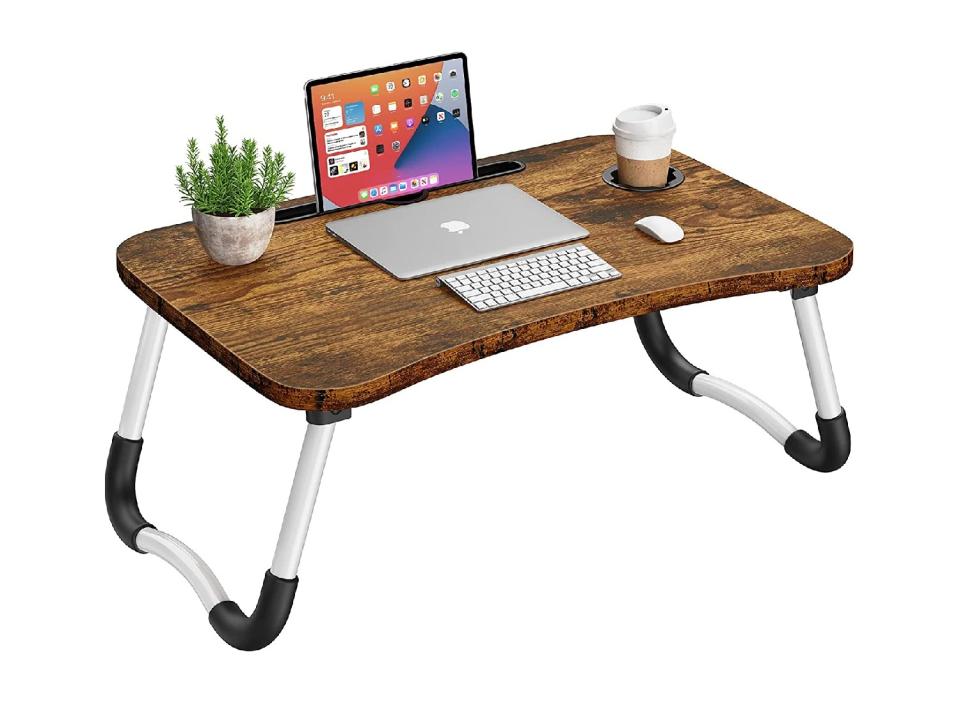 A bed-desk with a laptop, keyboard, cupholder, potted planet and mouse atop it.