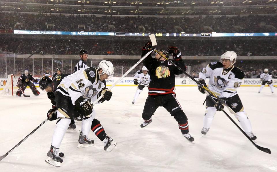 Chicago Blackhawks center Jonathan Toews is hit in the face by a high stick from Pittsburgh Penguins left wing Chris Kunitz (14) as Michal Rozsival (32) and Sidney Crosby (87) watch during the first period of an NHL Stadium Series hockey game at Soldier Field on Saturday, March 1, 2014, in Chicago. (AP Photo/Charles Rex Arbogast)