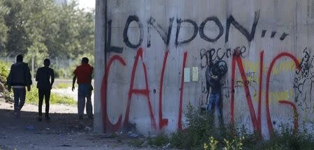 Migrants are seen in silhouette as they walk past the message, "London Calling" near the make-shift immigrant camp, called the jungle, in Calais, France, after Britain's referendum results to leave the European Union were announced June 24, 2016. REUTERS/Pascal Rossignol