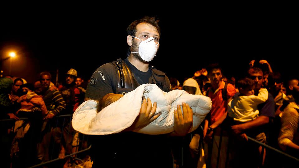 A Greek policeman holds a Syrian refugee child as a crowd of refugees and migrants wait to cross at Geece's border. Photo: REUTERS/Yannis Behrakis