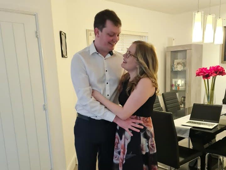 Mikhalia and her partner, Scott, holding each other while leaning against a dining table in a kitchen.