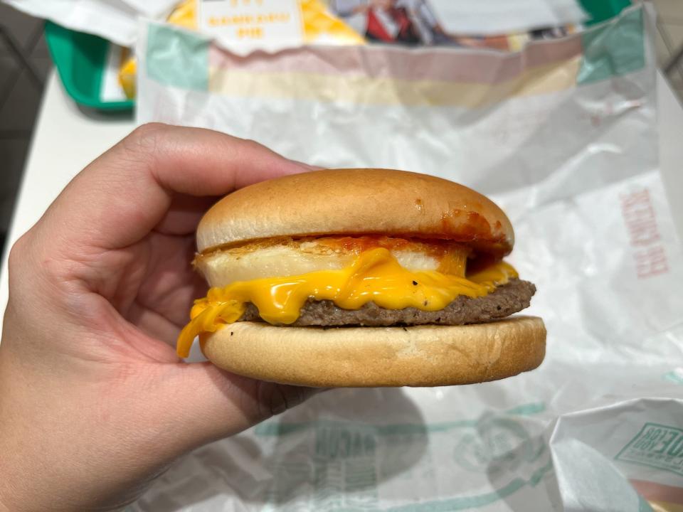 A hand holding a burger on a bun with egg and cheese,