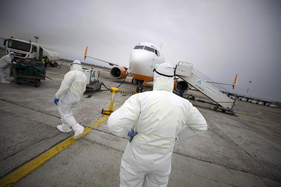 In this handout photo provided by the Ukrainian Presidential Press Office, A group of medical personnel stand ready at the Ukrainian aircraft chartered by the Ukrainian government for evacuation from the Chinese city of Wuhan, lands at Borispil international airport outside Kyiv, Ukraine, Thursday, Feb. 20, 2020. The plane carrying evacuees from Wuhan, including over 45 Ukrainians and a number of foreign passengers landed ahead of a 14-day quarantine in the country. (Ukrainian Presidential Press Office via AP)