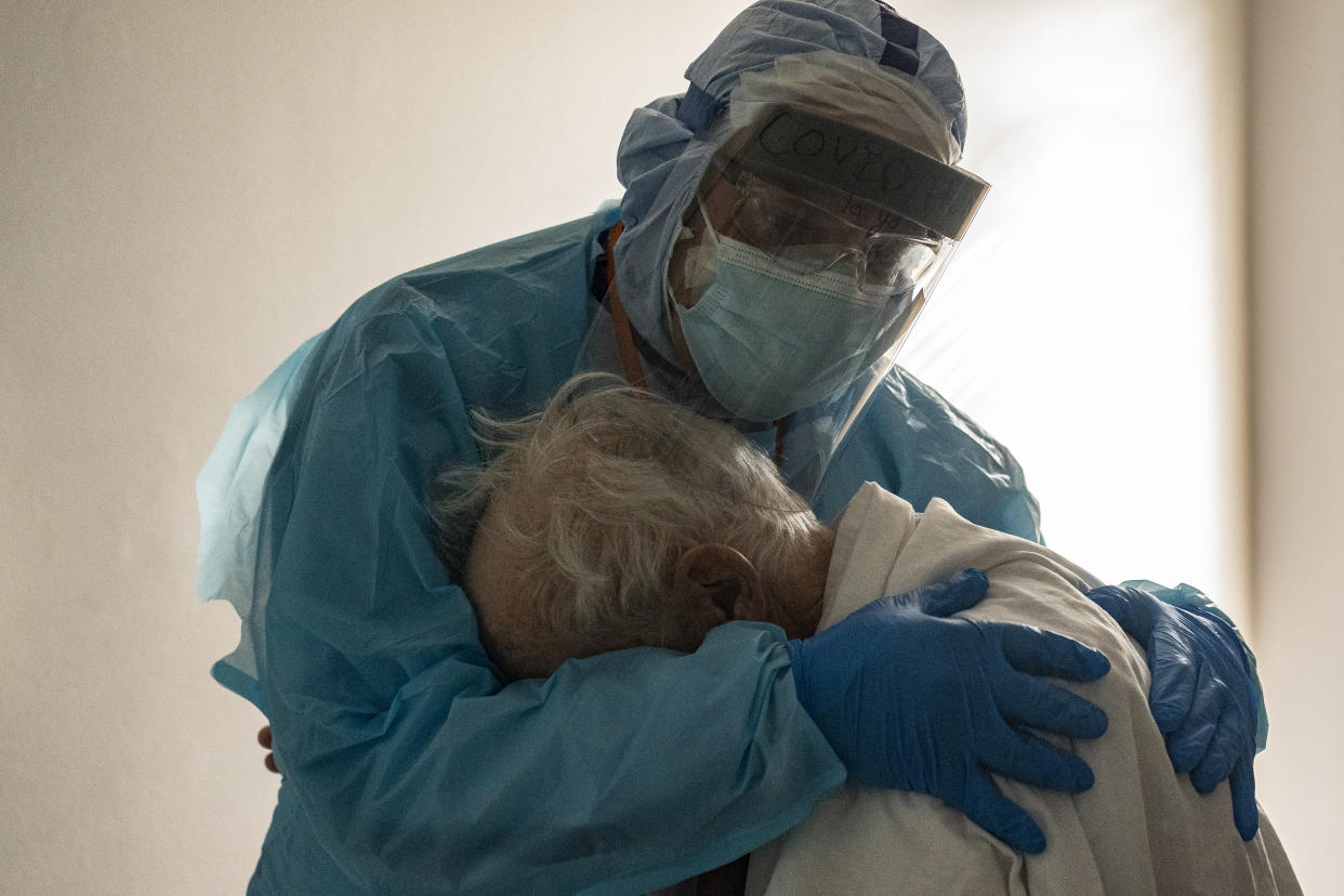Dr. Joseph Varon, wearing rubber gloves, a visor, mask and blue plastic scrubs, hugs a patient.