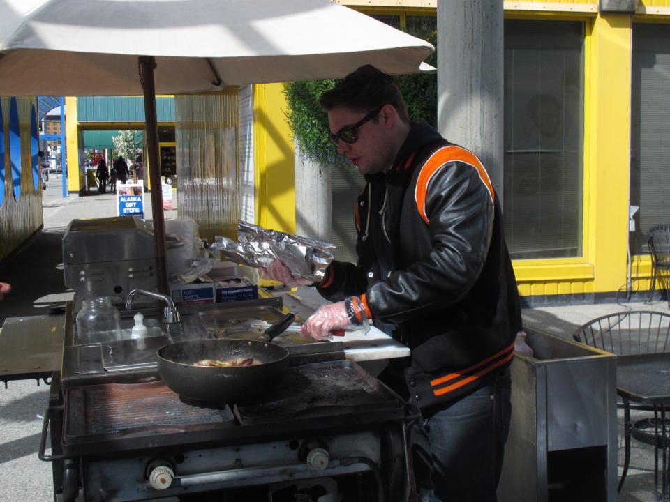 In this photo taken Thursday, May 31, 2012, in Anchorage, Scott Root of Anchorage tends to a customer at a downtown hot dog stand. Travel and Leisure poll readers have named Anchorage residents as the nation's worst-dressed. New York came in tops in the poll. Root says when you go to New York, you want to dress to impress at the fancy hotspots. But in Anchorage, Root said you dress differently because "it's all outdoors." (AP Photo/Mark Thiessen)