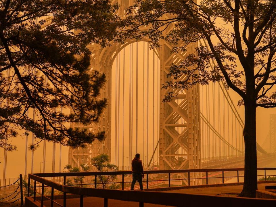 A man talks on his phone as he looks through the haze at the George Washington Bridge in Fort Lee, N.J., June 7, 2023.