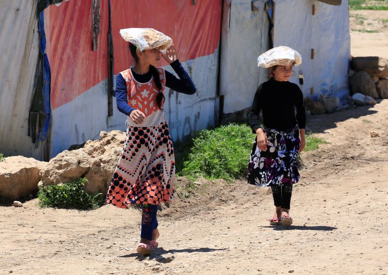 Syrian refugee girls carry stacks of bread on their heads, as Lebanon extends a lockdown to combat the spread of the coronavirus disease (COVID-19) at a Syrian refugee camp in the Bekaa valley