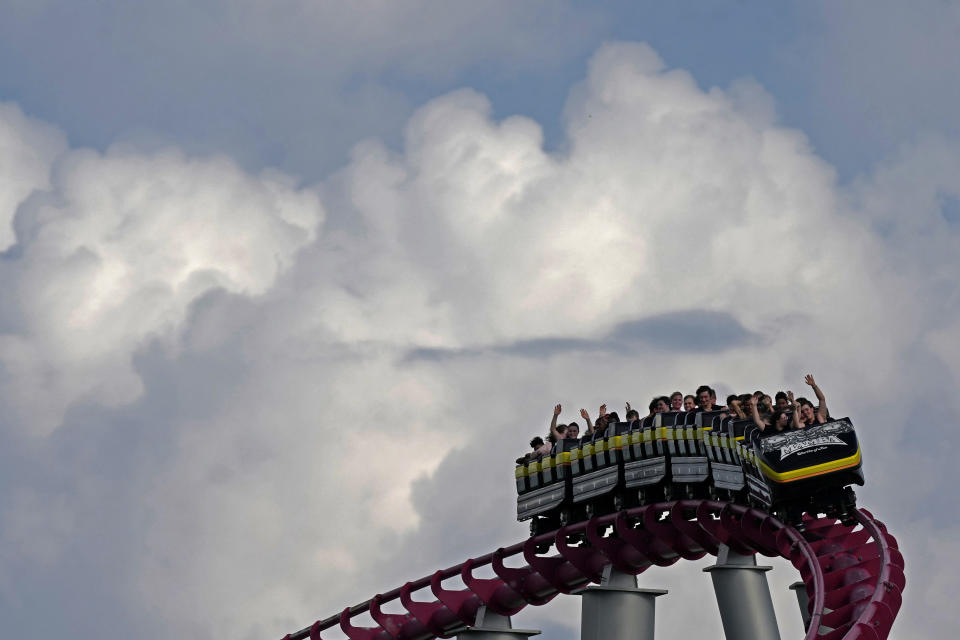 People ride on the Mamba roller coaster at Worlds of Fun theme park as storm clouds build in the distance on the first full day of summer Friday, June 21, 2024, in Kansas City, Mo. (AP Photo/Charlie Riedel)