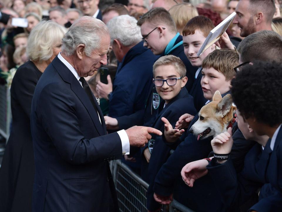 King Charles III points at a corgi in a crowd.