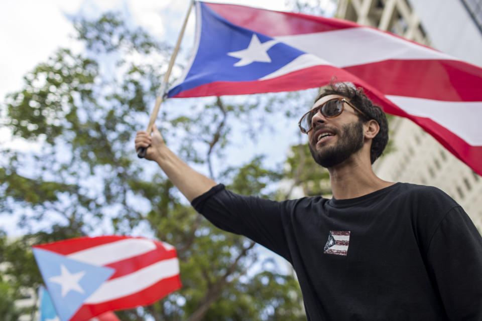 In this July 25 photo, a demonstrator flies a Puerto Rico flag as people gather to celebrate the resignation of Gov. Ricardo Rossello who announced that he is resigning Aug. 2, after weeks of protests over leaked obscene, misogynistic online chats, in San Juan, Puerto Rico. Puerto Rico's leaderless movement has drawn students, professionals, retirees, and rich and poor alike, and that's why they say it has been so successful. (AP Photo/Dennis M. Rivera Pichardo)