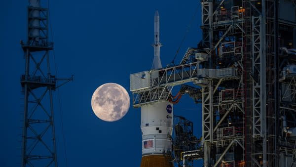  The full moon hangs in frame with the orion, inside its payload shell atop the SLS rocket. 