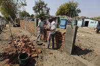 FILE- In this Feb. 17, 2020, file photo, workers construct a wall in front of a slum ahead of U.S. President Donald Trump's visit, in Ahmedabad, India. To welcome Trump, who last year likened Modi to Elvis Presley for his crowd-pulling power at a rally in Houston, the Gujarat government has spent almost $14 million on ads blanketing the city that show the two leaders holding up their hands, flanked by the Indian and U.S. flags. It also scrambled to build a wall to hide a slum from the road Trump and first lady Melania Trump will travel, caught stray dogs, planted exotic trees and is rushing to finish a cricket stadium in time for Trump’s arrival. (AP Photo/Ajit Solanki, File)