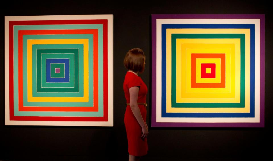 Ένας υπάλληλος της γκαλερί με δύο έργα της Στέλλας από τη δεκαετία του 1970, «Δ.  Scramble: Ascending Green Values/Ascending Spectrum», αριστερά και «I.  Scramble: Αύξουσα κίτρινη τιμή/φθίνον φάσμα'