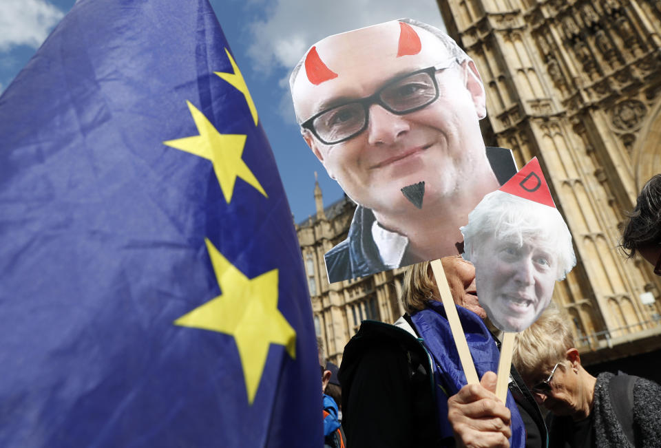 Remain supporters wave flags and hold signs with a photo of British Prime Minister Boris Johnson, right, and Special Advisor to British Prime Minister Boris Johnson, Dominic Cummings, left, during a demonstration outside the gates of Parliament in London, Wednesday, Sept. 4, 2019. With Britain's prime minister weakened by a major defeat in Parliament, defiant lawmakers were moving Wednesday to bar Boris Johnson from pursuing a "no-deal" departure from the European Union. (AP Photo/Alastair Grant)