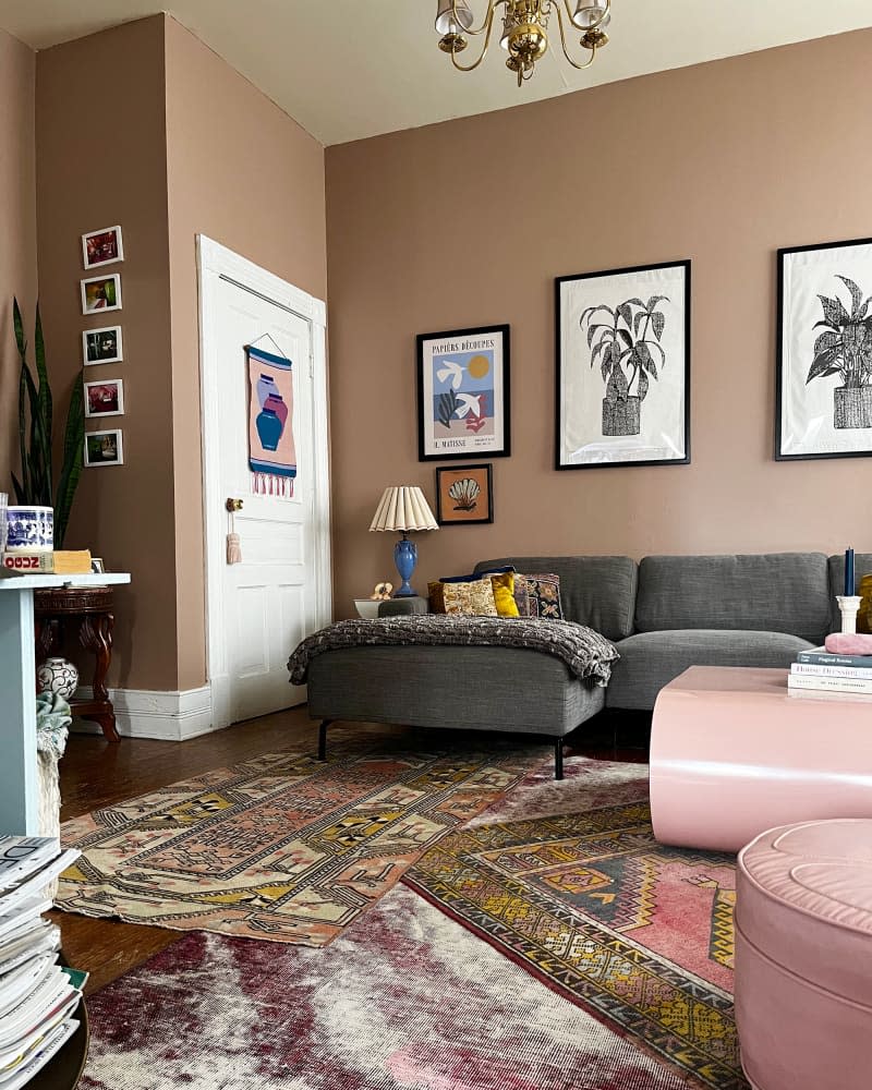 Gray sofa sits atop multiple area rugs in living room featuring art hung on pink brown walls.