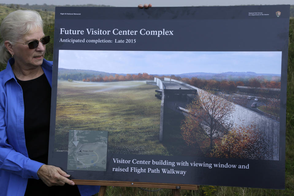 Friends of Flight 93 volunteer ambassador Charlotte Jones holds an artist's rendering of the 450-foot-long Flight 93 National Memorial visitor center complex before a ground breaking ceremony on Tuesday, Sept. 10, 2013, in Shanksville, Pa. The 6,800 foot visitor center is designed so that the building will be broken in two at the point of the plane’s flight path, and is expected to open in late 2015. The ridge will be built up to give people a clear view of the crash site, which is near a memorial wall that lists the names of all 33 passengers and seven crew members who were killed. Flight 93 was traveling from Newark, N.J., to San Francisco on Sept. 11, 2001, when it was diverted from the likely goal of crashing it into the White House or Capitol. (AP Photo/Gene J. Puskar)