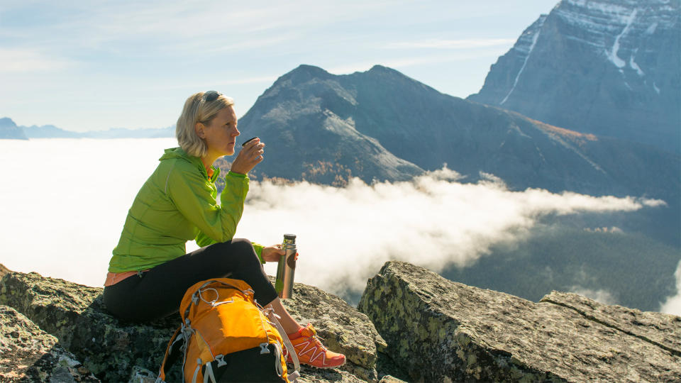 Woman sitting on mountain drinking from insulated flask