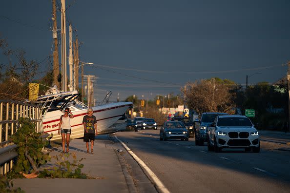 People walk along a sidewalk blocked by boats after Hurricane Ian on September 29, 2022, in Bonita Springs, Florida.