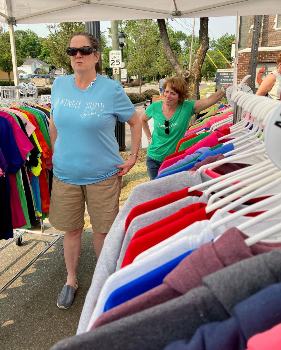 Mary Alice Flanagan-Conser, a retired special ed teacher from Novi, tries on a T-shirt in Mary Keyser's booth at  Art on The Grand in downtown Farmington on Sunday, June 4.