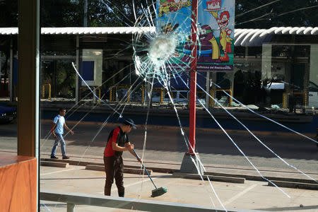 A broken restaurant window is seen after being looted while an employee sweeps the pavement, caused by the delayed vote count of he presidential election in Tegucigalpa, Honduras December 2, 2017. REUTERS/Jorge Cabrera