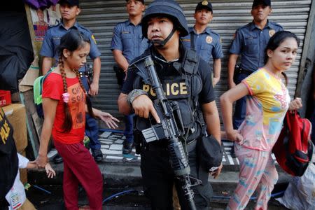 A policeman holds his weapon as people pass by during a drug raid in Quezon City, Metro Manila, Philippines, October 12, 2016. REUTERS/Damir Sagolj