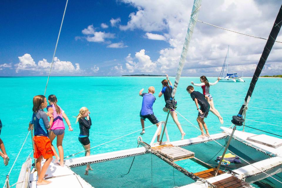Kids jumping off a boat into turquoise waters.