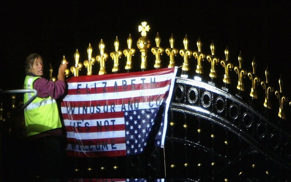 Percy is hanging a defaced US flag on the gates, wearing a hi-vis vest