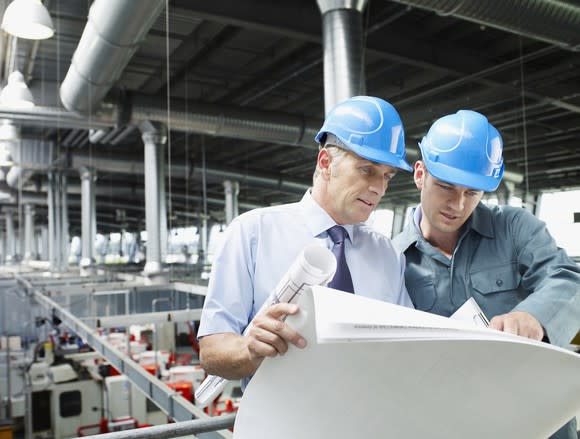 Two men looking at blueprints above a factory floor